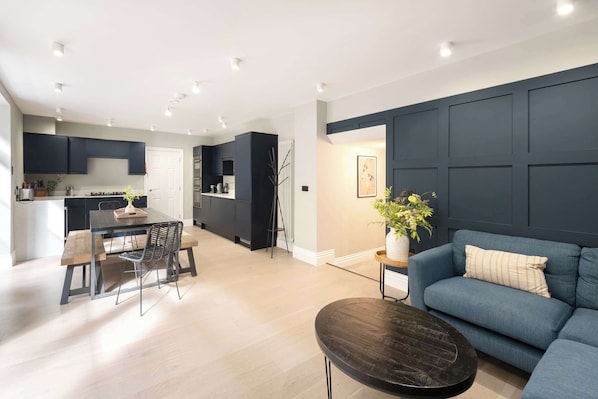 Una sala de estar moderna con un sofá azul oscuro, una mesa de centro redonda y un comedor con mesa y sillas de madera.