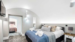 A modern bedroom with a curved ceiling, a bed with a blue blanket, white pillows, and a nightstand with a lamp.
