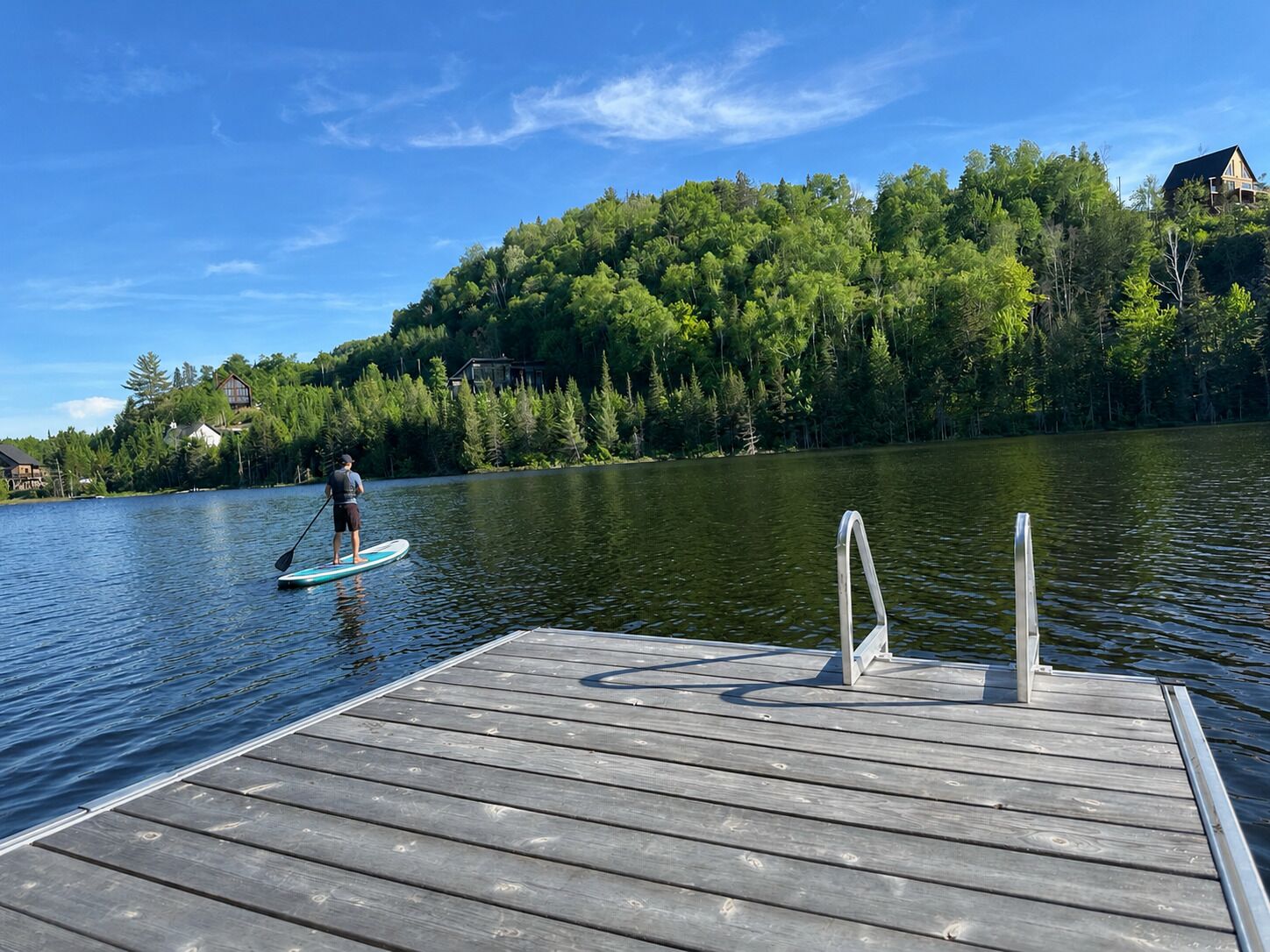 A wooden dock extending into a calm lake with a person paddleboarding.