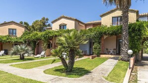 Une rangée de villas de style méditerranéen, dotées d’espaces extérieurs aménagés, de palmiers et surplombant un ciel d’un bleu éclatant.