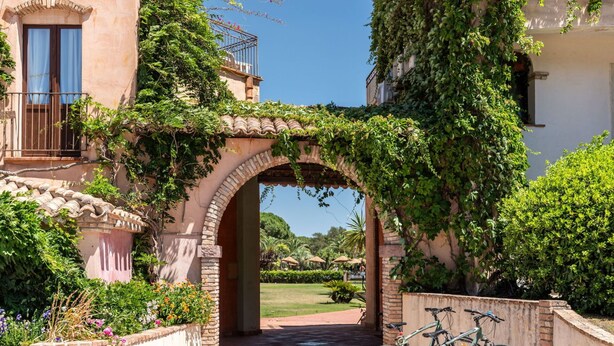 Une entrée extérieure avec une arche en briques, une terrasse carrelée et des vélos garés.