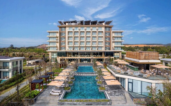 Un hotel moderno con varios pisos, una piscina central y zonas de estar al aire libre.