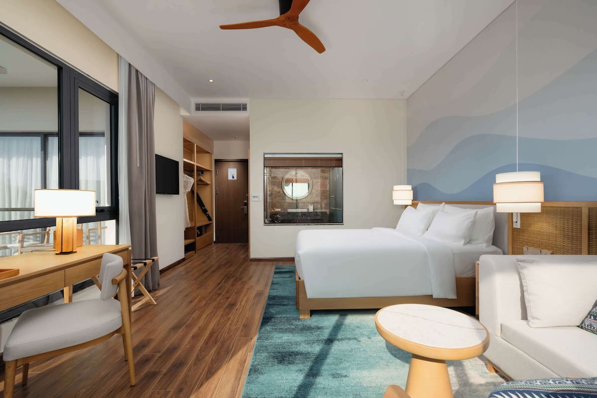 A hotel room with a bed, a desk, a chair, a sofa, and a ceiling fan.