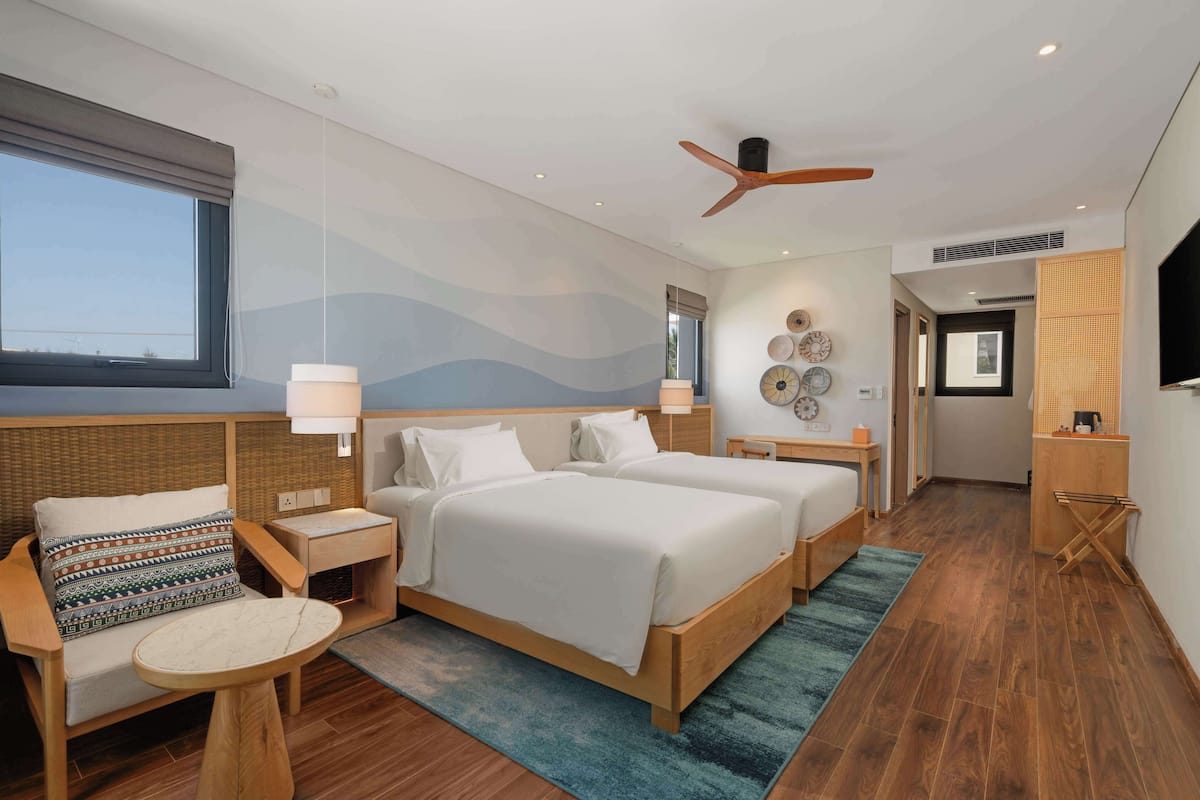 A modern hotel room with two beds, a sitting area, a TV, and a ceiling fan.