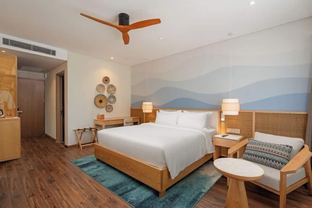 A hotel room with a wooden bed, a round table, a chair, and a ceiling fan.