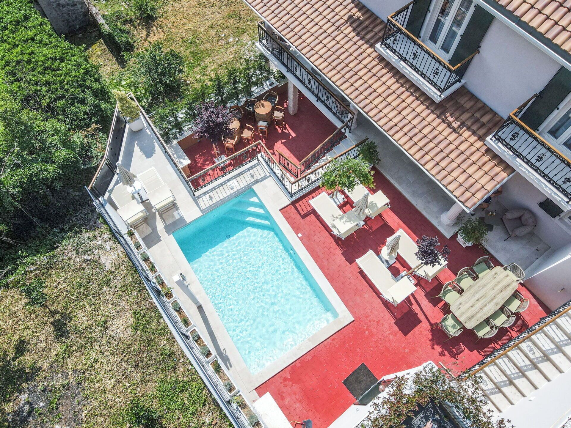An aerial view of a hotel with a swimming pool, outdoor seating, and a red-tiled roof.