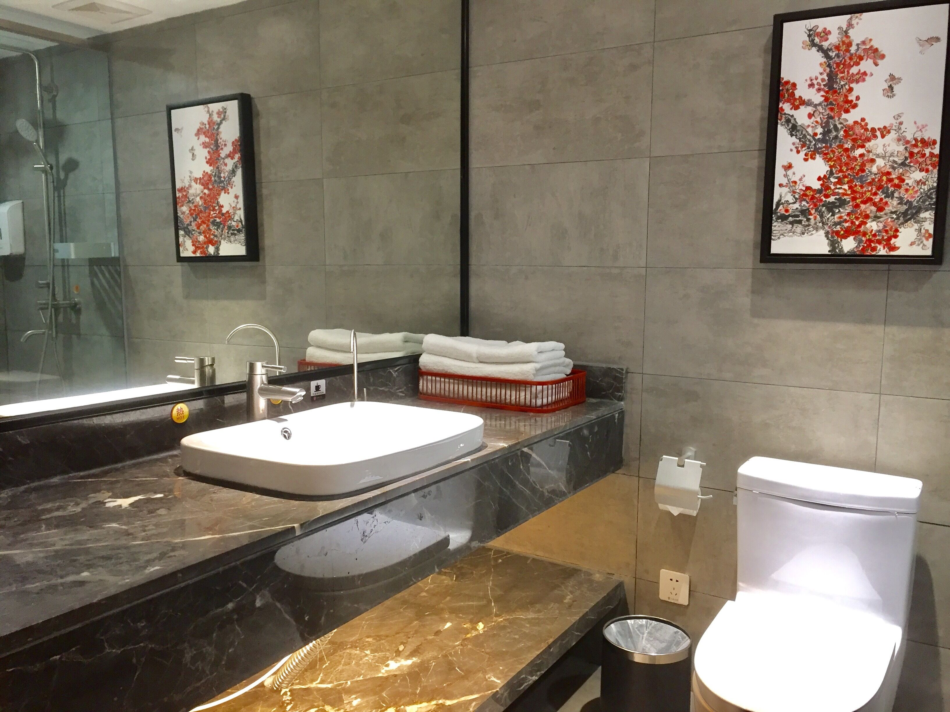 A modern bathroom with a large mirror, a sink, a toilet, and a trash bin.