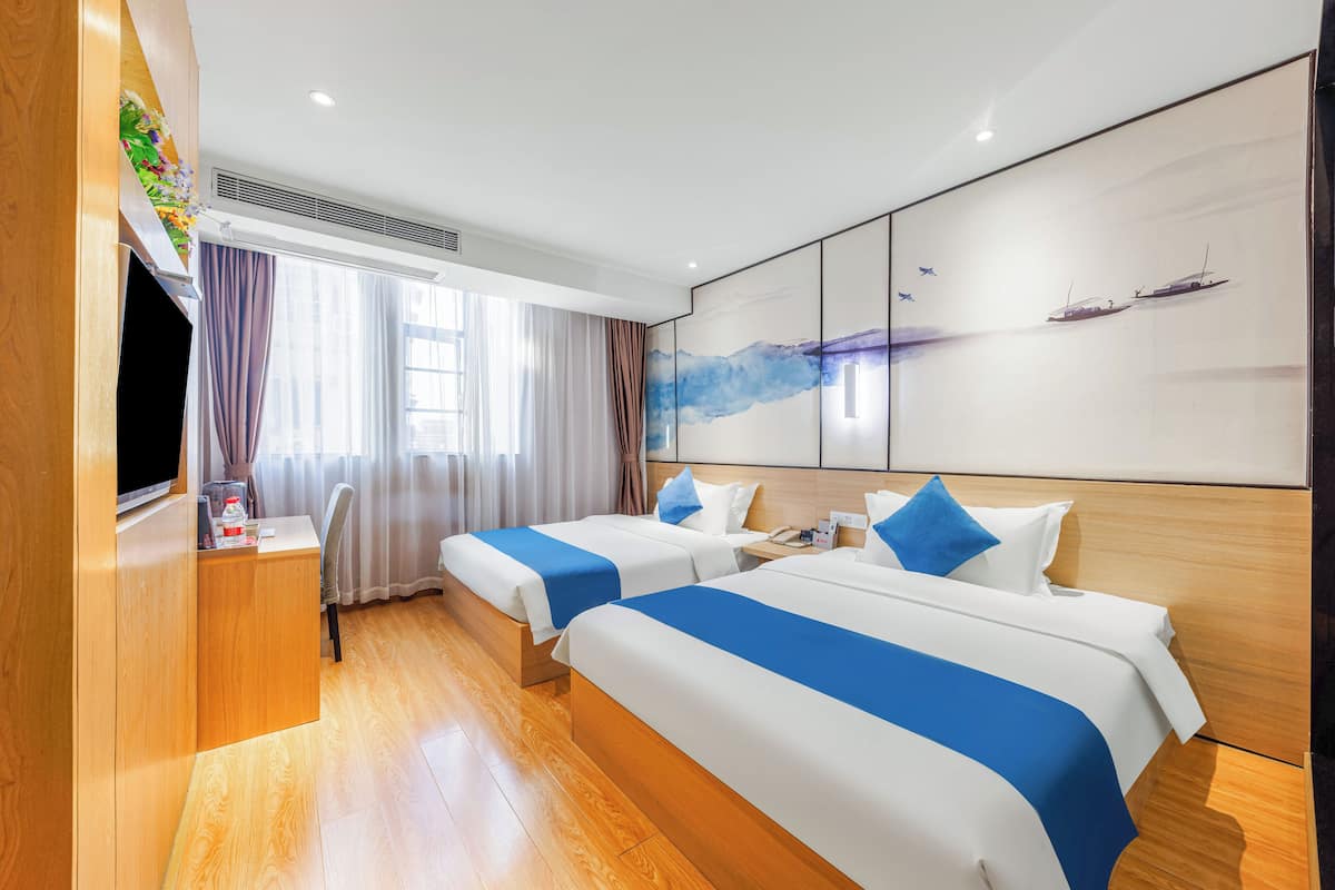 Habitación de hotel con dos camas, un escritorio, televisión y un amplio ventanal con cortinas.