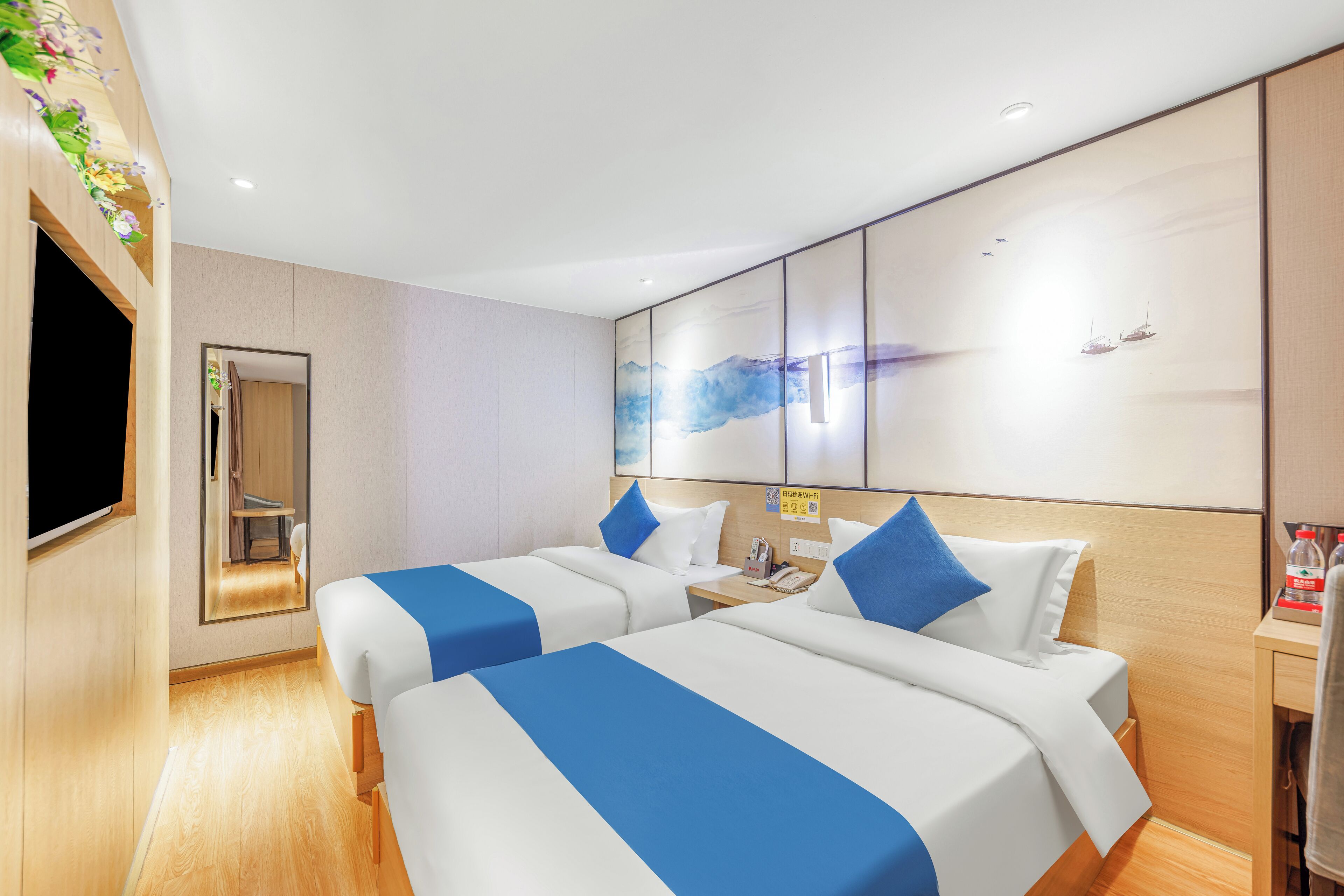Een hotelkamer met twee bedden, een televisie, een spiegel, een houten vloer en een muur met een schilderij.