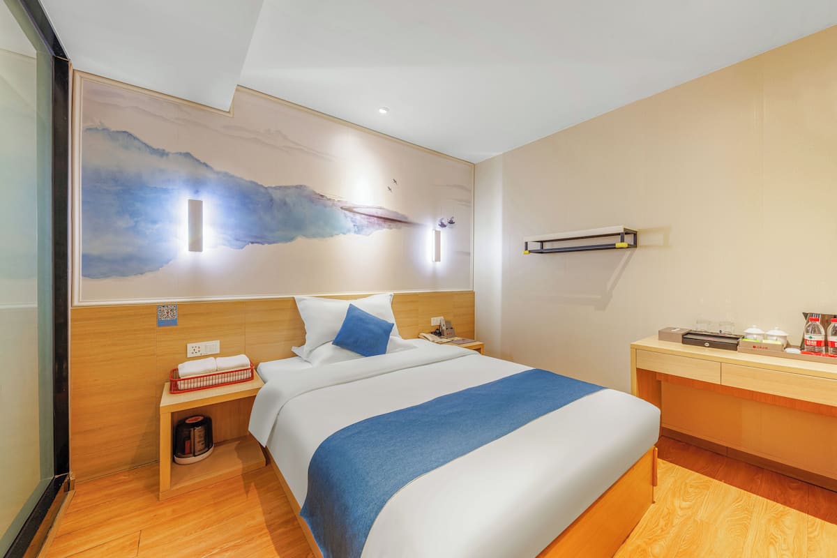 Una habitación de hotel con una cama, una mesita de noche, un escritorio y una pared con un cuadro.