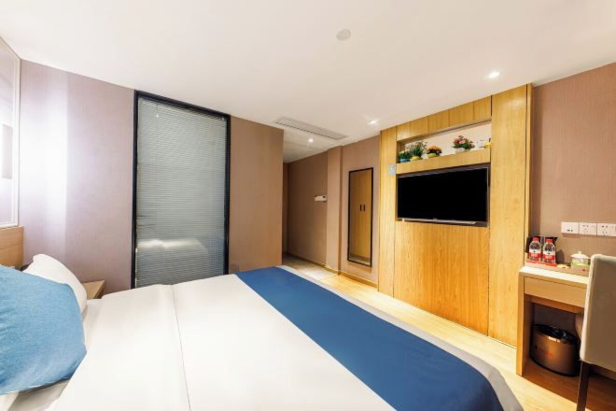 Habitación de hotel con cama, escritorio, televisión y ventana con persianas.