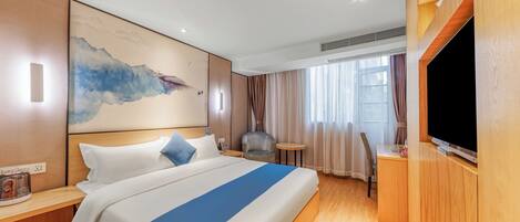Quarto de hotel com uma cama grande, uma escrivaninha, uma televisão de tela plana, uma cadeira e uma pequena mesa.
