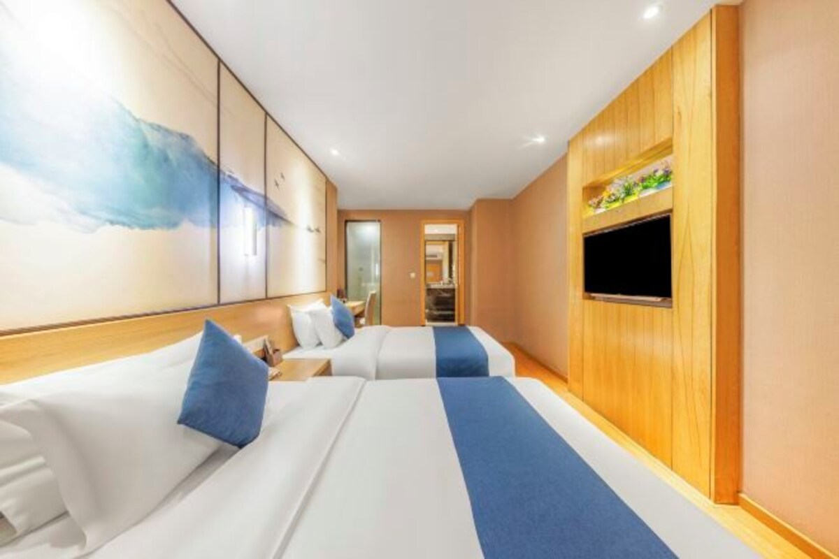 Una habitación de hotel con dos camas, un televisor montado en la pared y detalles de panel de madera.