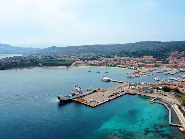 A coastal town with a marina, clear waters, and a hilly backdrop.