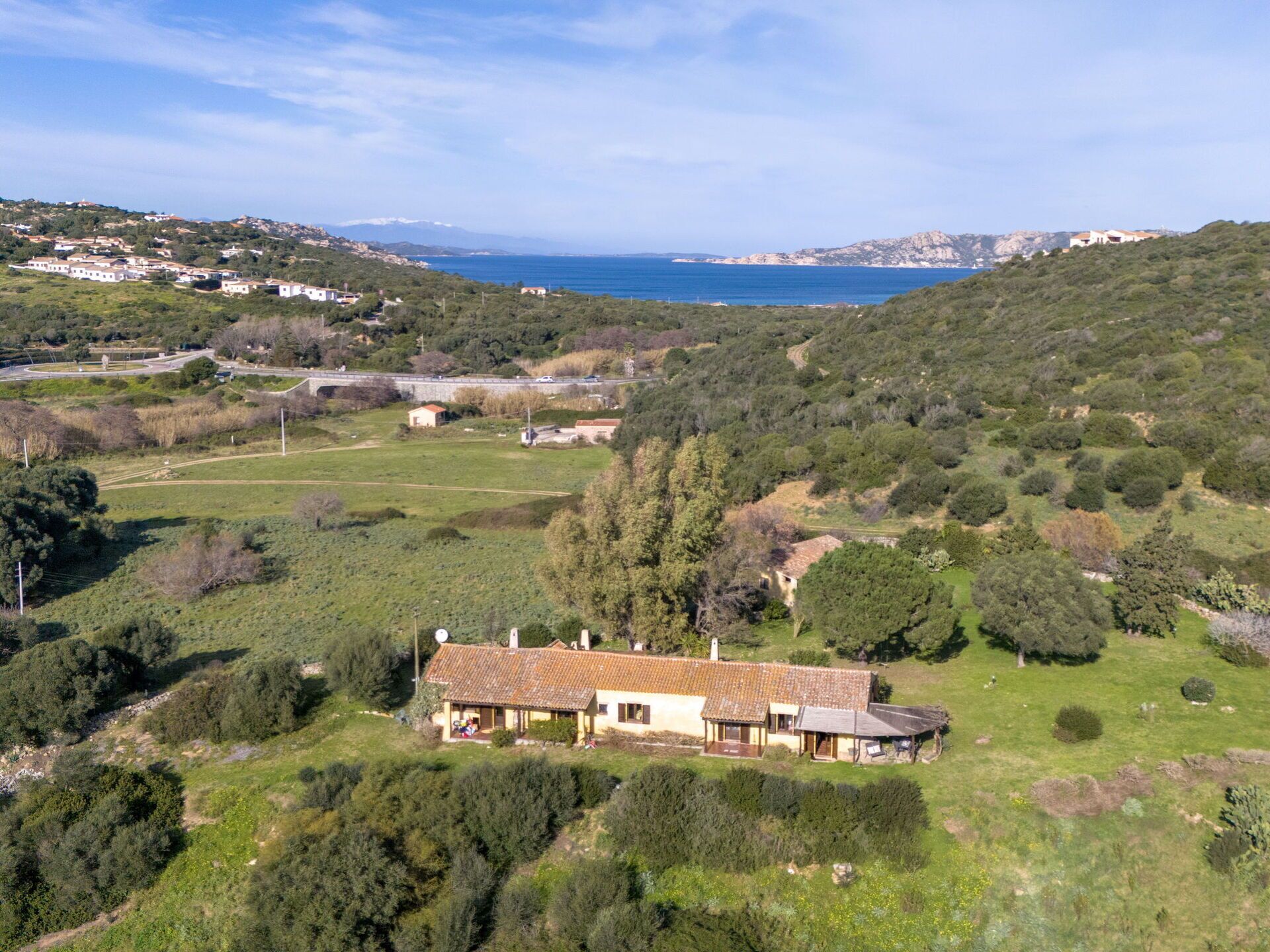 Una casa rural con tejado de tejas, rodeada de vegetación y vistas al mar.