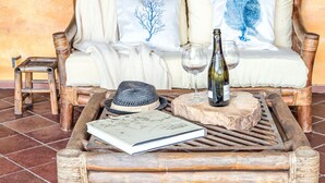 A wicker coffee table with a book, a bottle, and glasses on it, placed in front of a sofa with decorative pillows.