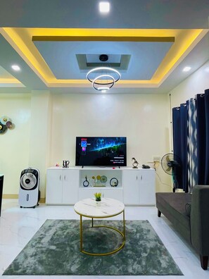 A modern living room with a flat-screen TV, white cabinets, a round coffee table, a standing fan, and a grey sofa.