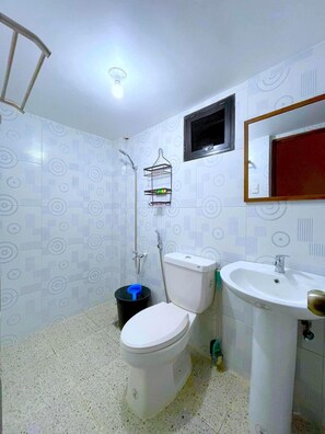 A bathroom with a toilet, sink, shower, and a small window.