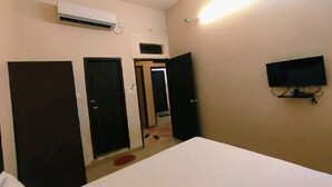 Een hotelkamer met een bed, een airconditioning, een televisie en drie deuren.