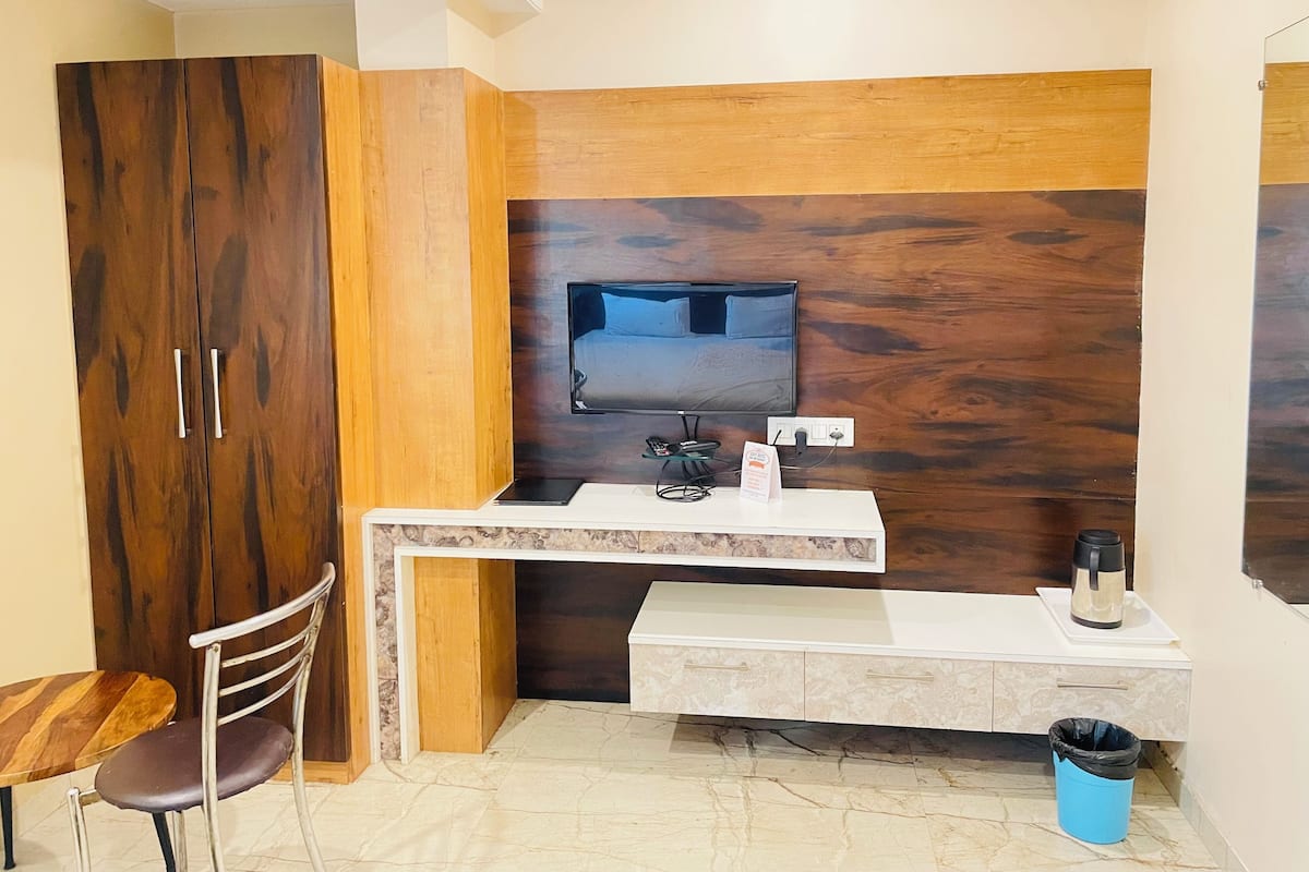 A compact room with a wooden wardrobe, a small desk with a TV, a chair, and a coffee machine.