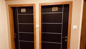 Two black doors with wooden frames and a white stripe in the center, labeled with room numbers 104 and 105. - Gopi Hotel And Restaurant (Sagwara)