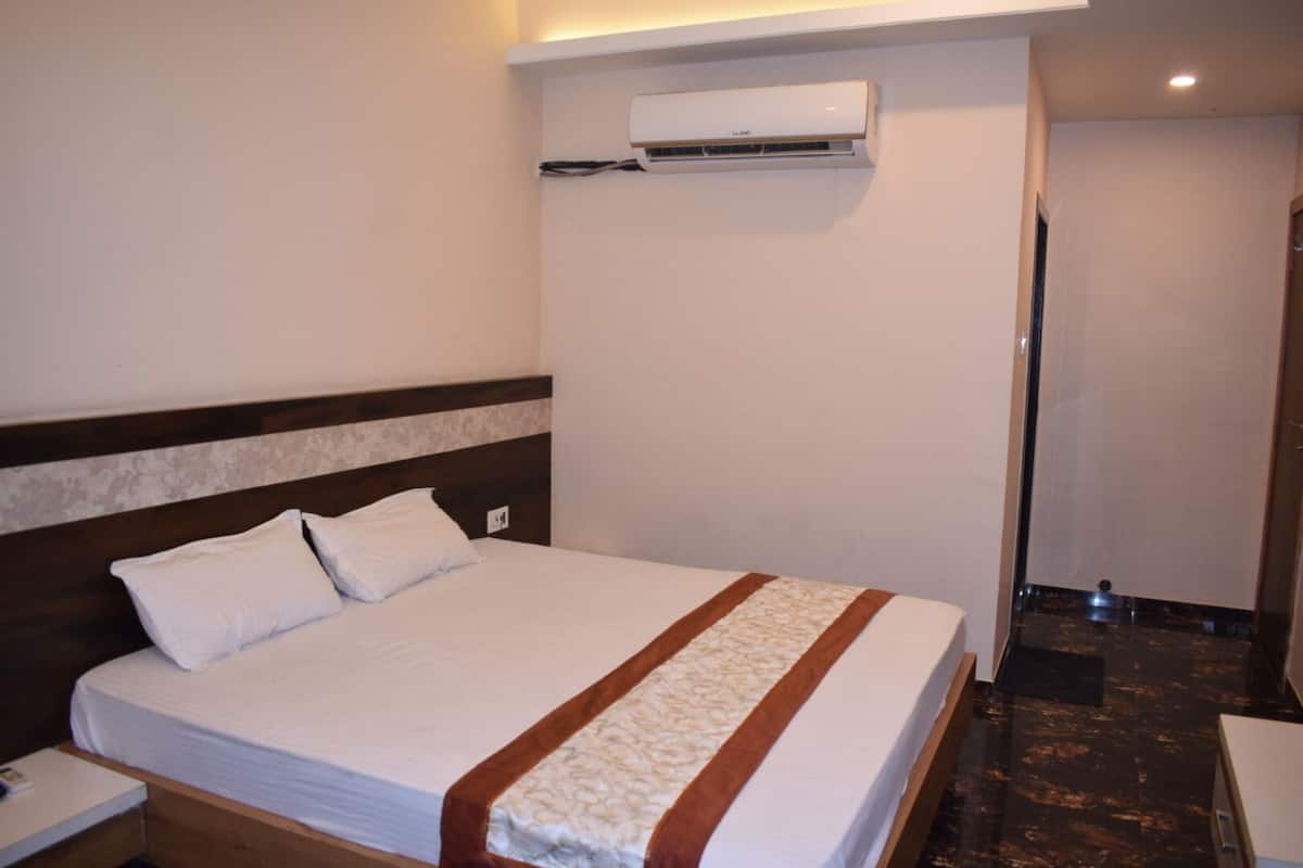 A hotel room with a bed, a nightstand, an air conditioning unit, and a bathroom door.