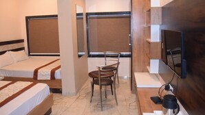 A hotel room with two single beds, a small table with chairs, a TV mounted on the wall, and a coffee maker on the floor. - Gopi Hotel And Restaurant (Sagwara)