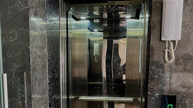 An elevator with a marble wall, a lift sign, a phone, and a digital display. - Gopi Hotel And Restaurant (Sagwara)