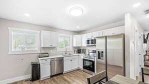 A modern kitchen with white cabinets, stainless steel appliances, and a dining area with a table and chairs. - Renovated Urban Oasis in Indy (Indianapolis)