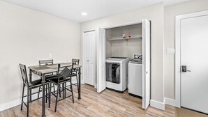 A compact kitchen with a dining table and chairs, a washer and dryer, and a white door. - Renovated Urban Oasis in Indy (Indianapolis)