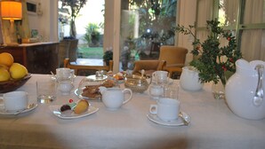 A dining table set with white tea cups, saucers, a teapot, and various pastries. - Volta House (Palermo)