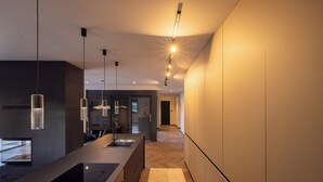 Une cuisine moderne dotée d’un long plan de travail, d’appareils électroménagers intégrés, de luminaires suspendus et d’un parquet en bois disposé en chevrons.