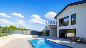 Une maison moderne dotée d’une piscine, de mobilier d’extérieur et d’un mur en pierre.