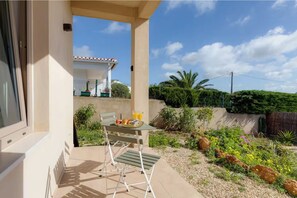 Un balcon avec une table préparée pour le petit-déjeuner, une chaise et une vue sur une maison avec un toit en tuiles.