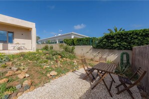Une terrasse avec une table et des chaises, entourée d’un jardin où poussent différentes plantes et bordée d’un chemin de gravier.