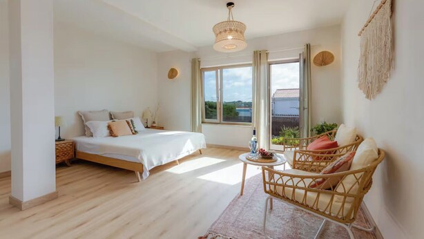 A bedroom with a bed, bedside table, and a wicker chair with cushions. - Eco Stay on the Hill by Sea N' Rent (Vila do Bispo)