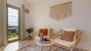 A room with two wicker chairs, a small round table with a bottle and glasses, a macrame wall hanging, a potted plant, and a view through a large window. - Eco Stay on the Hill by Sea N' Rent (Vila do Bispo)