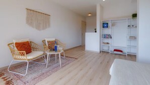 A modern living room with wicker chairs, a small round table, a macrame wall hanging, and a white shelving unit with books and decorative items. - Eco Stay on the Hill by Sea N' Rent (Vila do Bispo)