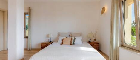 Una camera da letto con un letto grande, due comodini, una finestra con tende e vista sul verde.