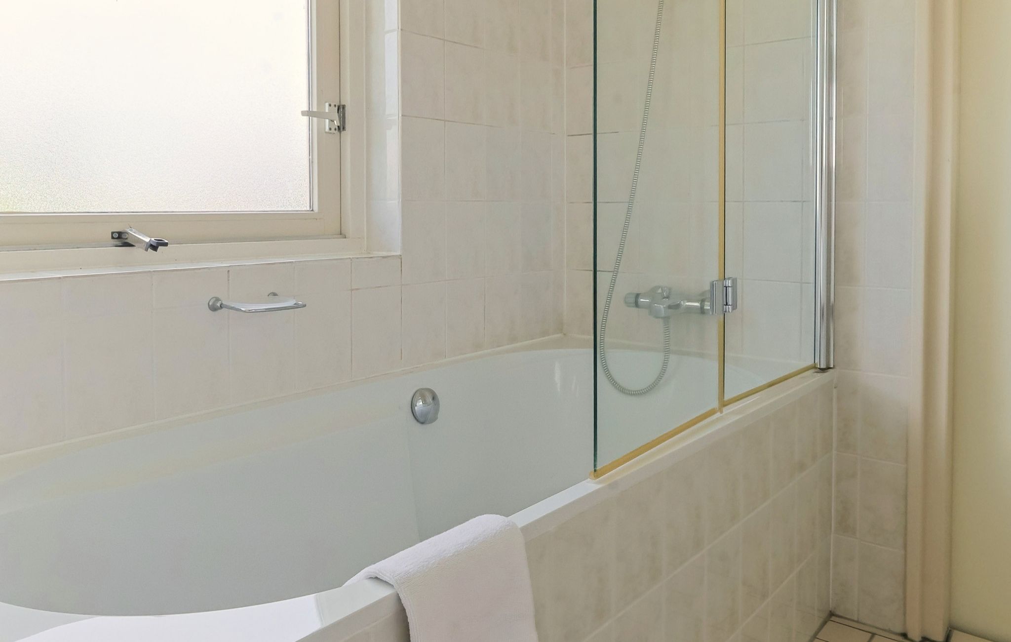 A modern bathroom with a glass-enclosed shower, a white bathtub, and a window above the sink.