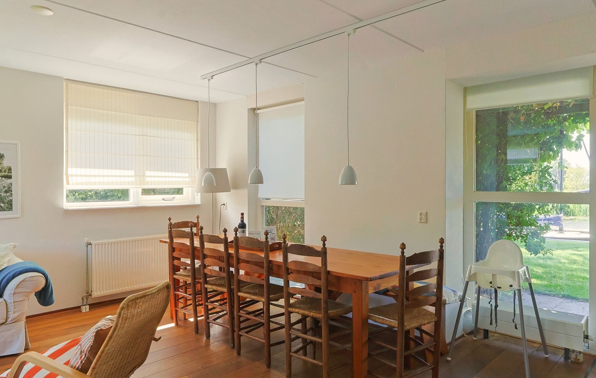 Een eetruimte met een houten tafel en stoelen, een radiator en een raam met zonwering.