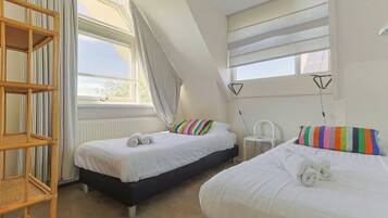 A room with two beds, a window, a radiator, and a chair.