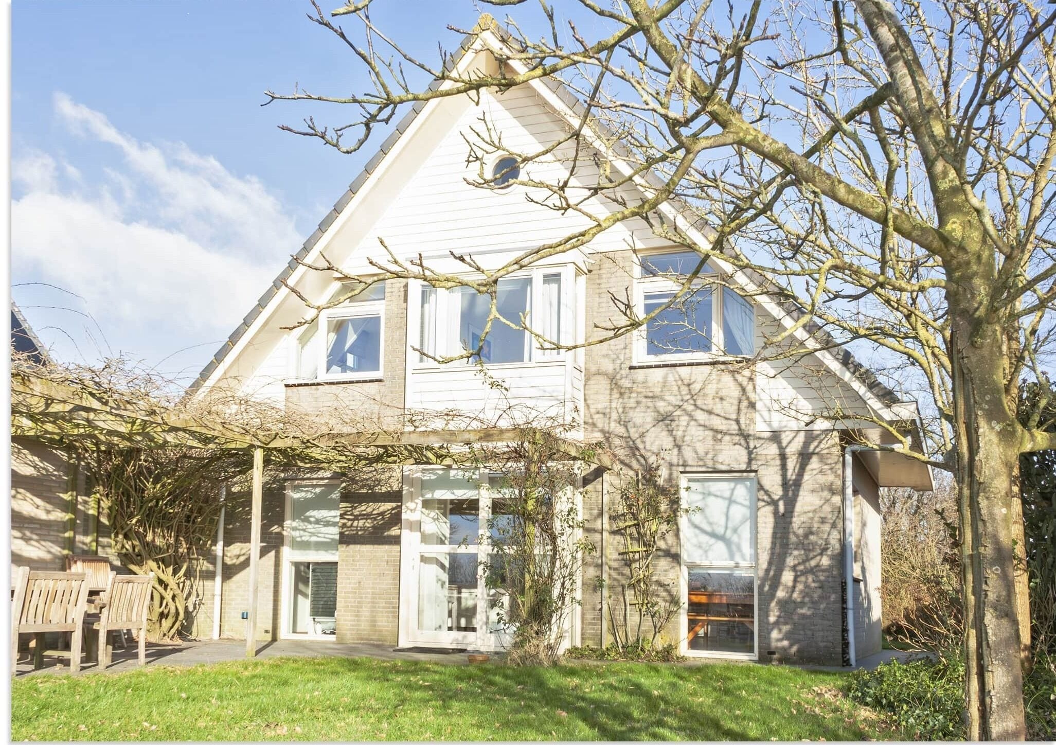 Ein zweistöckiges Haus mit überdachter Veranda und einem großen Baum im Vordergrund.