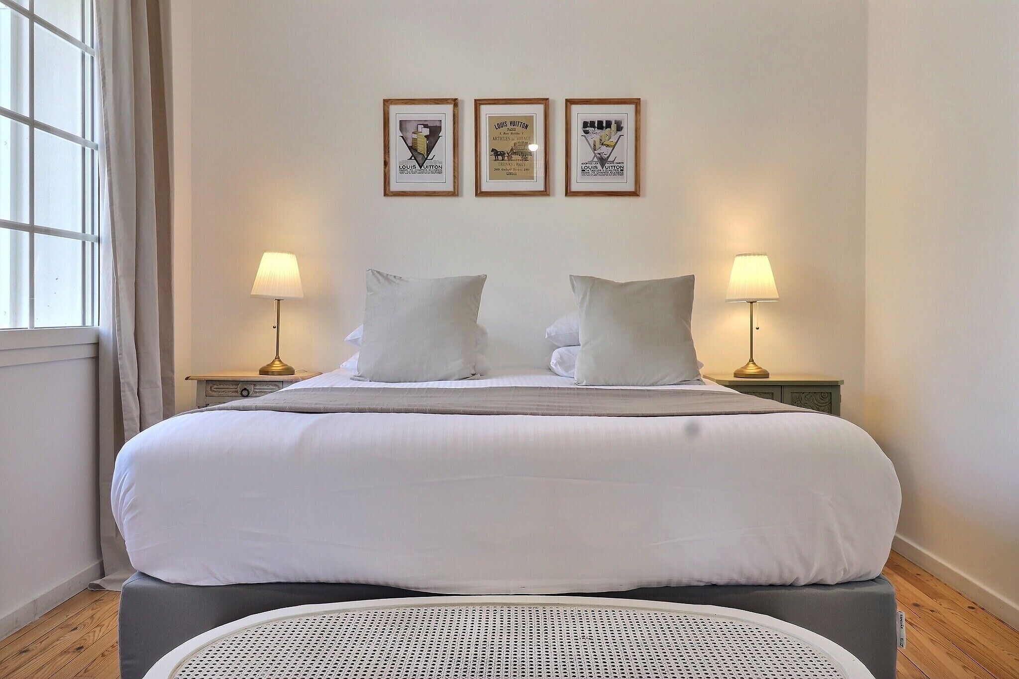 A neatly made bed with white linens, two bedside lamps, and three framed posters on the wall.
