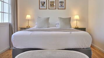 A neatly made bed with white linens, two bedside lamps, and three framed posters on the wall.
