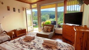 A bedroom with a bed, a chair, a dresser, a television, and a view of the outdoors. - Harmony of romance and nature for two, in a double bedroom (Miskolc)