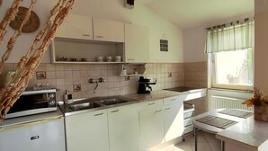 A kitchen with white cabinets, a microwave, a sink, and a window with a view. - Harmony of romance and nature for two, in a double bedroom (Miskolc)