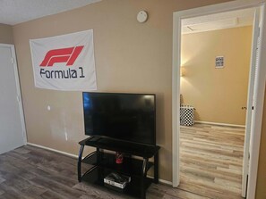 Ett rum med en Formel 1-banner, ett svart TV-bord och en svartvit papperskorg.