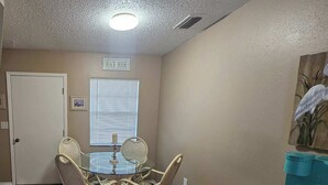 A dining area with a glass-top table and wicker chairs, a door labeled "BEACH HOUSE", and a window with blinds. - Professor Rousseau's Sea Turtle Sanctuary (Crystal River)