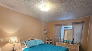 A bedroom with a bed, nightstand, lamp, dresser, and a window with curtains. - Professor Rousseau's Sea Turtle Sanctuary (Crystal River)